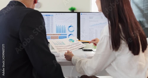 Analysts teamwork discuss finance data and dashboard. Colleagues review charts on computer screens and printouts, aligning analytics with metrics. Concept image of collaborative office analysis.