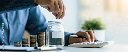 Person stacking coins and adding to a jar, calculator nearby