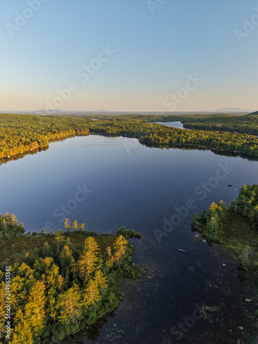 Foto Aerial view of an Egg Pond in Lincoln, Maine surrounded by dense forest bathed in golden hour light with mirror-like water reflections