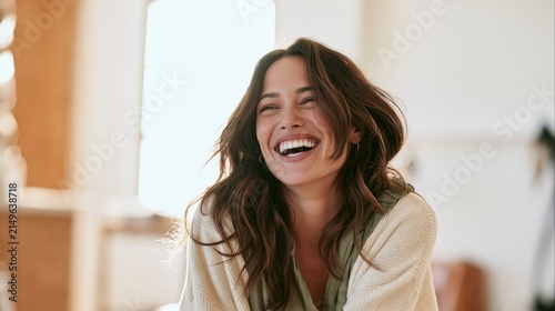 Candid editorial style lifestyle portrait of a young woman laughing happily indoors.