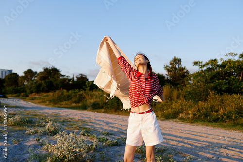 Bild auf Leinwand Smiling woman outdoors on a sunny day, wearing a red striped top and white shorts, waving a scarf in the breeze