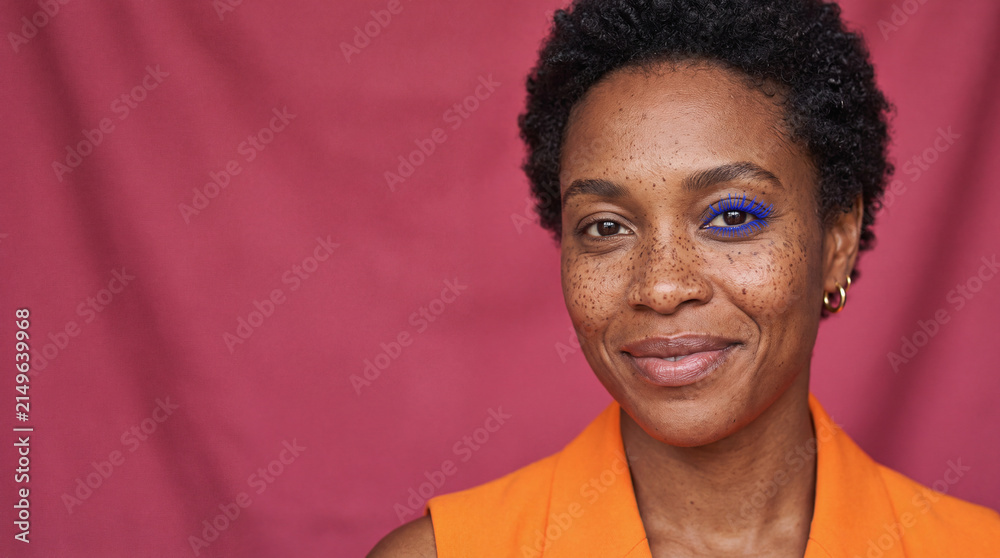 Obraz premium Woman smiling with blue mascara showing diverse beauty and freckles on a vibrant pink background
