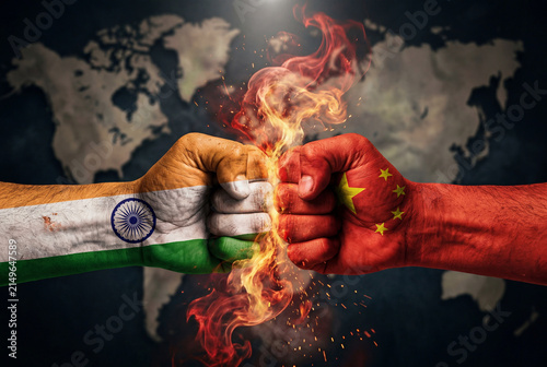 Two fists painted with flags of india and china clashing together with fire against a world map