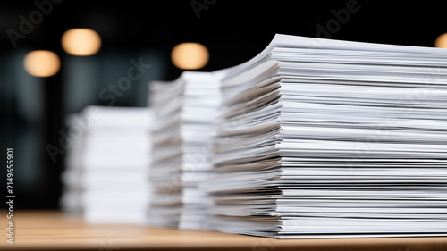 Stacks of paper documents on a desk represent administrative workload and organized business records.
