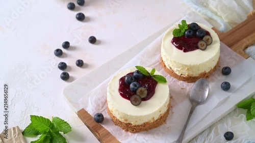 Top view of creamy mini cheesecakes featuring a smooth texture and crumbly crust under bright natural lighting, garnished with glossy berry compote and fresh mint.