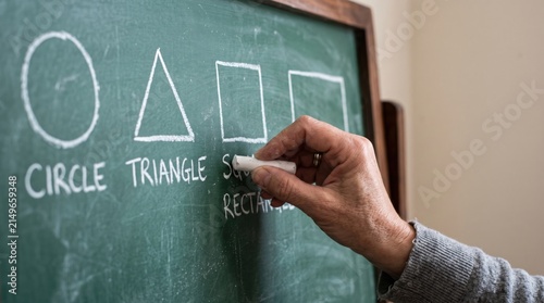 Close up of a teacher's hand holding chalk and drawing geometric shapes on a classic green chalkboard in a school classroom