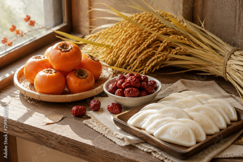 Persimmons, dried jujubes, half-moon rice cakes and rice stalks on window ledge, serene harvest still life