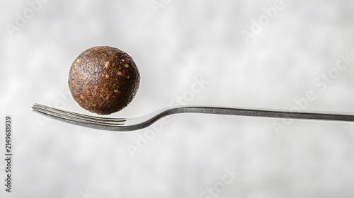 Single Healthy Protein Energy Ball or Meatball Balanced on a Silver Fork Over White Background