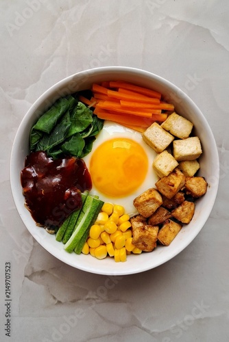 Bibimbap, a vibrant Korean rice dish topped with a variety of seasoned vegetables, gochujang, and a fried egg, often accompanied by sliced meat. Mixed together, it creates a flavorful and balanced.