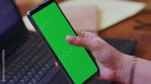 Hand Holding Smartphone with Green Screen Over Laptop