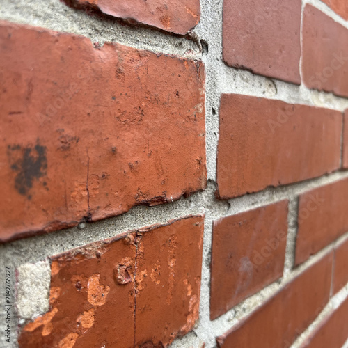 A close up view of an old red brick wall showing weathered texture, cracked mortar, and uneven surfaces in a vertical composition during daylight