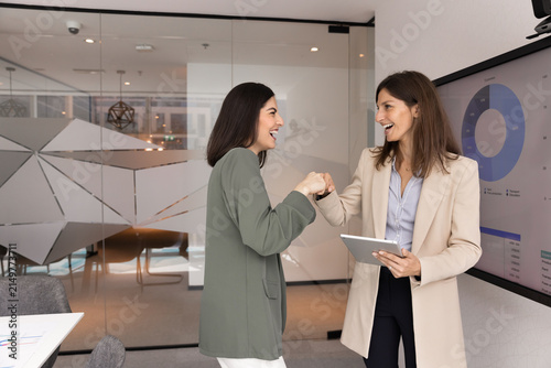 Fotografie Two happy diverse women corporate colleagues confirming strategic partnership with fist bump on meeting in conference room celebrating project milestone showing trust agreement alliance