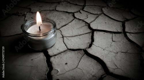 Candle burning giving light on cracked dry earth