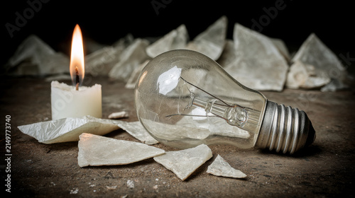 Candle flame illuminating broken incandescent light bulb fragments