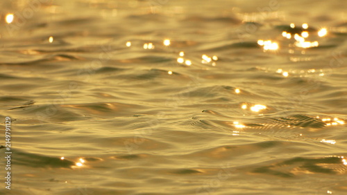 Golden water sparkles reflecting sunset light on the calm ocean surface with copy space