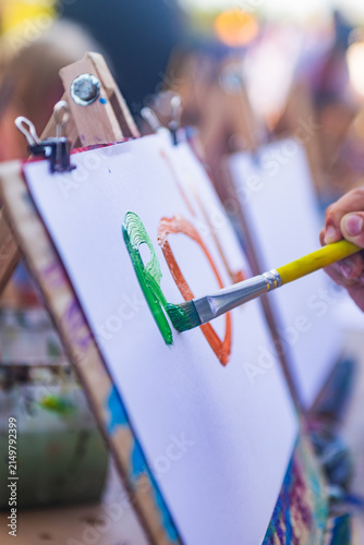 Close-up of Child's Hand Painting on Canvas on a Wooden Easel