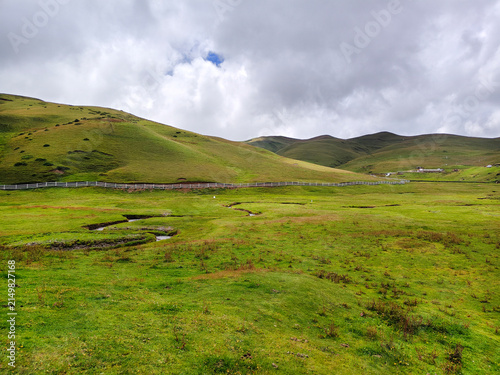 A scenic landscape view of the Small Rhinoceros  viewpoint at Dahai Caoshan (Dahai Grassland) in Huize, Qujing, Yunnan, China. Winding river stream flowing through the lush green rolling h