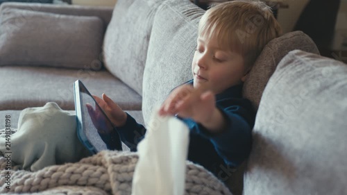 Sick boy blowing his nose watching tablet on sofa
