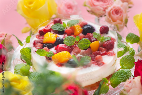 ピンクの背景に映えるベリーとフルーツのケーキと色鮮やかなバラの花々