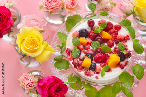 ピンクの背景に映えるベリーとフルーツのケーキと色鮮やかなバラの花々