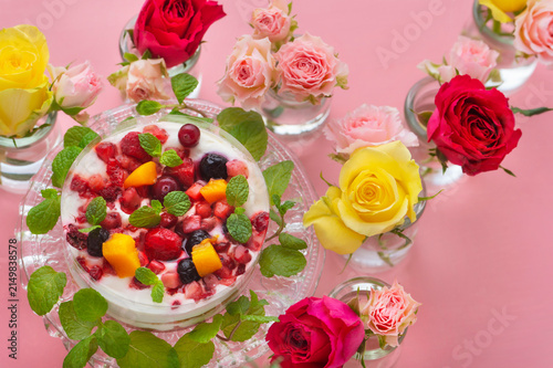 ピンクの背景に映えるベリーとフルーツのケーキと色鮮やかなバラの花々