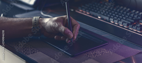 Moody atmospheric shot of a digital artist working on a graphic tablet with a stylus in a studio