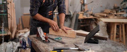 Bild auf Leinwand Professional Carpenter Measuring Wooden Board at Workbench in Woodworking Worksh