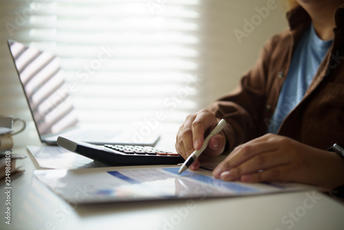 Person reviewing financial documents with calculator, pen, and laptop at a home office desk, representing budgeting, accounting, and personal finance planning.