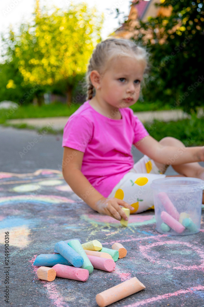 Fototapeta premium Little girl draws with colorful chalk on the asphalt on the street in summer