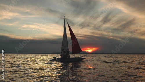A crewed sailing catamaran moves across a lake at sunset, in slow motion.