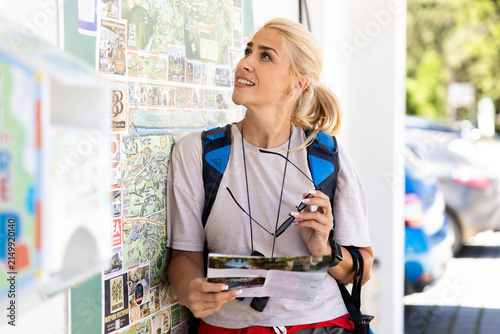 Cuadro en lienzo Blonde woman traveling, carrying a backpack and holding sunglasses, studying a m