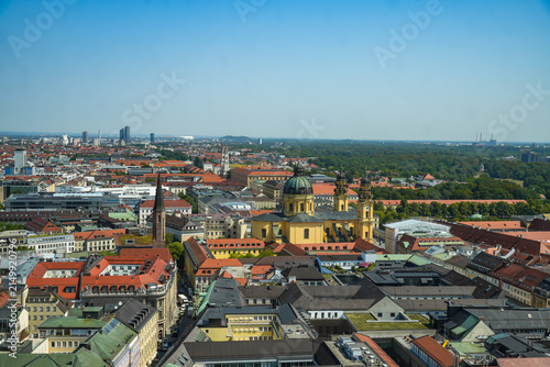 Aerial view of Munich featuring the striking yellow Theatine Church, Odeonsplatz, and the English Garden on the horizon. Taken from the tower of the Frauenkirche on a sunny summer day.