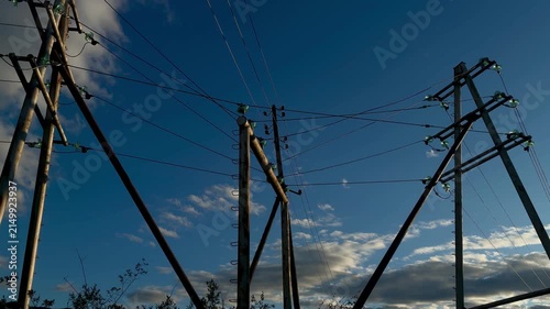 Dramatic low angle shot of high voltage electricity power lines and transmission pylons against a beautiful blue sky with clouds.