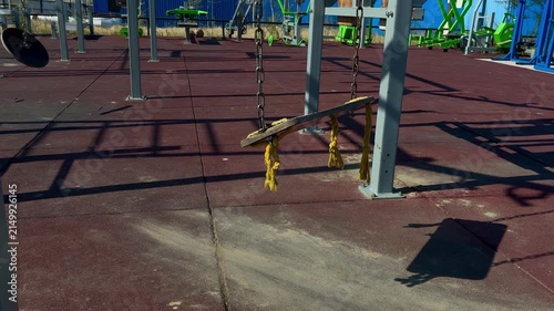Sunny day at an outdoor fitness park featuring a wooden swing on chains and various exercise machines on a rubberized safety surface.