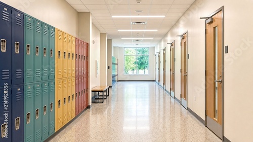 Empty school hallway with metal lockers lining both sides Long corridor in high school with rows of student lockers Educational institution hallway featuring storage lockers