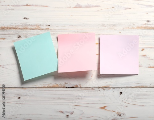 Three blank pastel sticky notes, blue, pink, and pale pink, on a white wooden surface