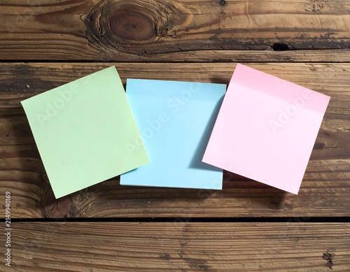 Three colorful sticky notes arranged on a textured, weathered wooden surface
