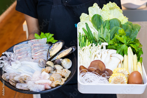 Waitress holding fresh raw seafood set and vegetable tray for hotpot or shabu shabu dining.