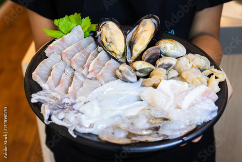Waitress holding plate of fresh raw seafood mix with fish slice squid mussels and shrimp for hotpot or shabu.