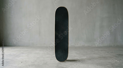 Black skateboard standing vertically against a plain gray concrete wall and floor, symbolizing urban culture, extreme sport, and freedom, free space for text