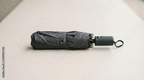 Dark gray compact umbrella with strap and handle, folded for portability, representing protection and preparedness for various weather conditions