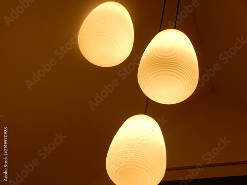 Cuadro en lienzo Vue en contre-plongée de trois luminaires suspendus aux formes arrondies diffusant une lumière chaude, créant une ambiance intérieure douce et chaleureuse