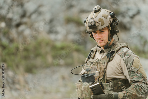 Outdoor military concept. Portrait of focused soldier wearing tactical gear looking calm with determined expression while training in rocky field environment