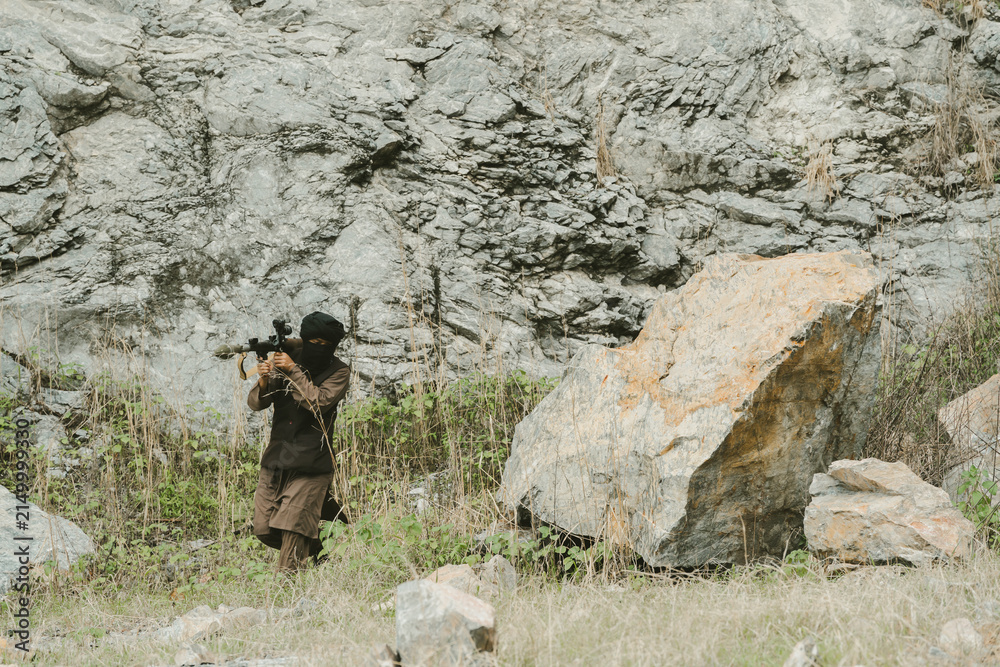 Obraz premium Outdoor military concept. Soldier with rifle focused in hostile terrain with intense expression, warrior alert during combat mission in rocky wilderness environment