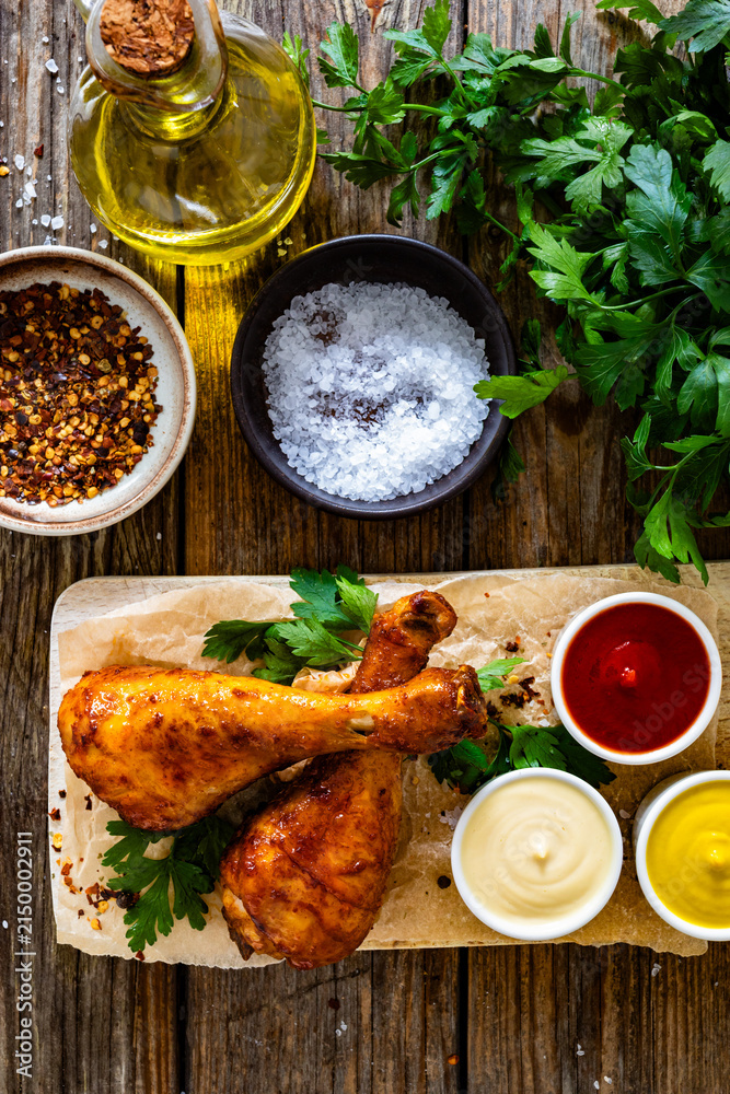 Fototapeta premium Air fryer chicken drumsticks with mayonnaise, ketchup and mustard on wooden table. Top view