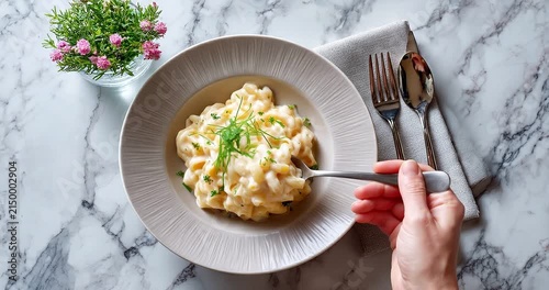 Gourmet pasta dish with creamy sauce served in a stylish ceramic bowl, top view of an elegant dinner setting on a marble table with fresh herbs and cutlery.