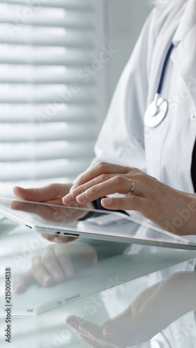 Healthcare professional wearing a lab coat and stethoscope, using a digital tablet for patient care, medical data management, and modern health technology