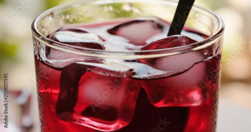 Close-up of a glass of chilled red fruit juice with ice cubes and a straw, refreshing summer beverage.
