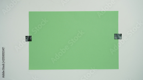 Foto A piece of green paper positioned vertical and attached to a surface with black tape on two sides, isolated on a white background