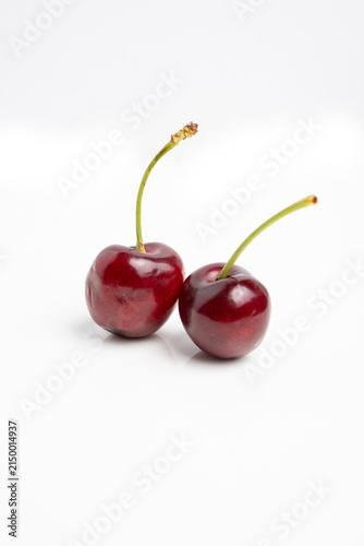 Pair of ripe cherries with glossy skin and green stems on white background, minimalist fruit photography highlighting color and texture